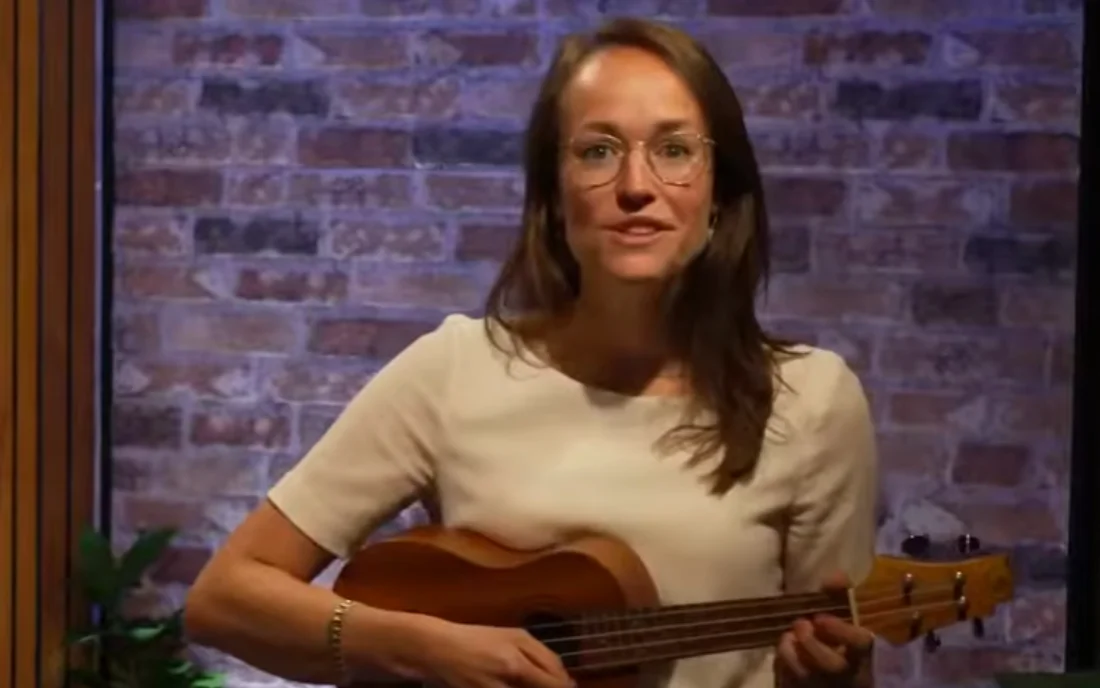 Isis met ukelele in de studio bij een bakstenen muur